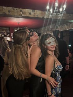 two women in masquerades are hugging each other at a party with people standing around