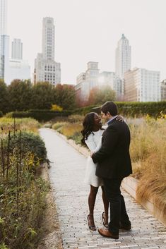 a man and woman standing next to each other on a brick walkway in front of tall buildings