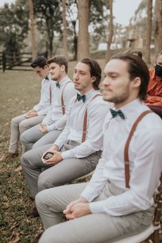 a group of men sitting next to each other on top of chairs in front of trees