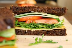 a sandwich with lettuce, carrots and other vegetables on it sitting on a cutting board