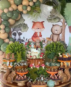 a birthday cake surrounded by plants and animals on a table with balloons in the background