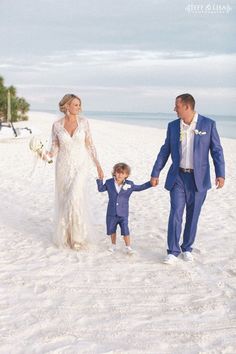 a bride and groom walking on the beach with their son holding his hand as he walks down the aisle