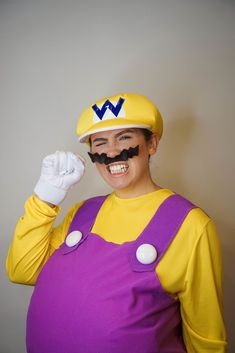 a woman in a yellow shirt and purple overalls with a mustache on her face