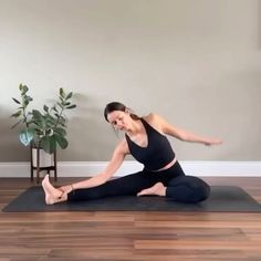 a woman is doing yoga on a mat in front of a potted plant with her legs spread out