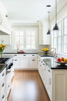 a kitchen with white cabinets and black counter tops, an island in the middle has fruit on it