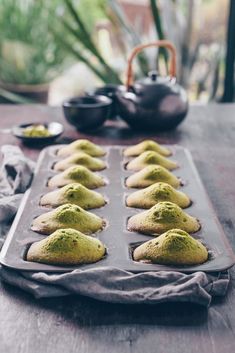 a pan filled with green powdered cookies on top of a wooden table next to potted plants