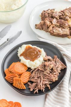 a black plate topped with meat, mashed potatoes and carrots