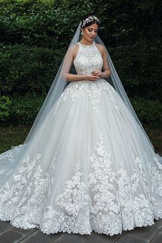 a woman wearing a wedding dress and veil standing in front of some bushes with her hands on her hips