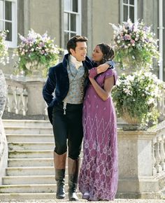 a man and woman standing next to each other in front of a building with flowers