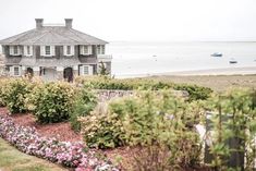 a large house sitting on top of a lush green field next to the ocean with boats in the water