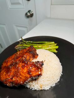 a black plate topped with rice and chicken next to asparagus on a counter