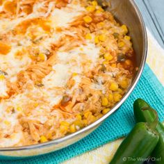 a casserole dish with corn, cheese and green peppers next to a blue towel