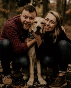 a man and woman pose with their dog in the woods