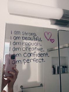 a woman taking a selfie in front of a bathroom mirror with writing on it