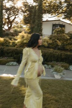 a pregnant woman in a yellow dress is walking through the grass with her hand on her hip