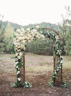 the wedding arch is decorated with white flowers and greenery for an elegant touch to the outdoor ceremony