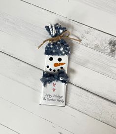 a snowman ornament hanging from a string on a white wooden background with the words happy holidays written below it