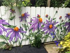 purple flowers painted on the side of a white fence with green leaves and orange centers