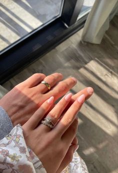 two hands holding each other with wedding rings on their fingers in front of a window