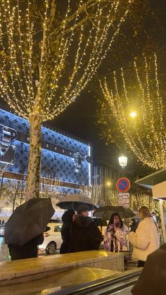 people standing under umbrellas in the rain on a city street at night with christmas lights