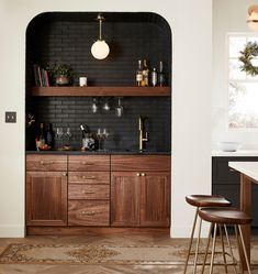 a kitchen with black brick wall and wooden cabinetry, gold accents and stools