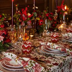 the table is set with red and white plates, silverware, flowers and candles