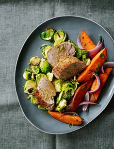 a plate filled with meat and vegetables on top of a gray table cloth next to a fork