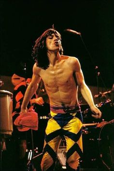 a man with no shirt on standing in front of a drum set and microphones