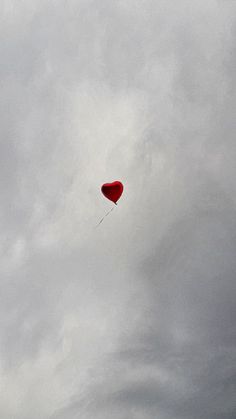 a red heart shaped kite flying in the cloudy sky