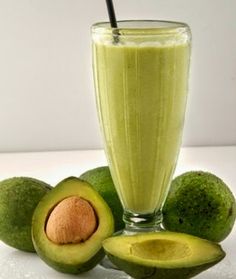 an avocado smoothie in a glass with a straw next to it and some sliced avocados