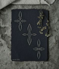 a piece of black paper with white designs on it next to dried flowers and leaves