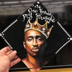 a hand holding up a graduation cap with a drawing of a man wearing a crown