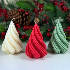 three different colored candles sitting on top of a table next to evergreen leaves and pine cones