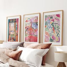 three paintings hang on the wall above a bed with white sheets and beige linens