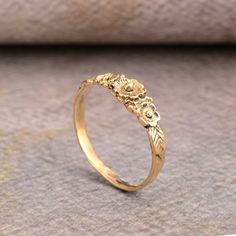 a gold ring with flowers and leaves on the side, sitting on top of a piece of fabric