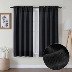 a black curtain hanging on the side of a window next to a white vase with flowers