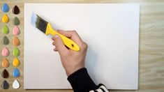 a person holding a paint brush over a piece of paper with colored drops on it