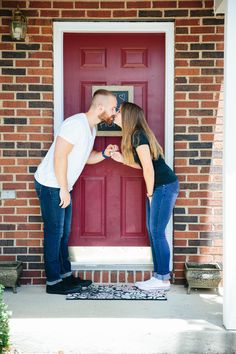 a man and woman standing in front of a red door with their hands on each other