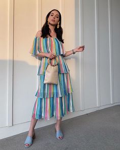 a woman standing in front of a white wall wearing a multicolored striped dress