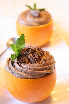 two oranges with chocolate frosting on them sitting on a white plate next to a spoon