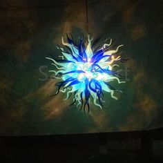 a blue and white light hanging from the ceiling in a dark room with clouds behind it