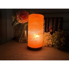 an orange himalayan candle sitting on top of a table next to some flowers and books