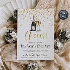 a new year's eve party with champagne and disco balls on the floor, next to a card that says cheers