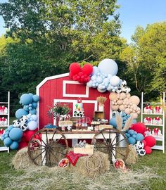 a red barn with balloons, hay bales and farm animals on the table in front of it