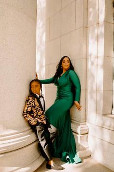 a woman in a long green dress leaning against a pillar next to a little boy