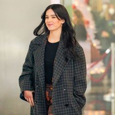 a woman is walking down the street wearing a black and gray coat with plaid pattern