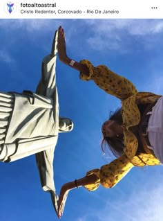 a woman standing next to a statue in front of a blue sky with white clouds