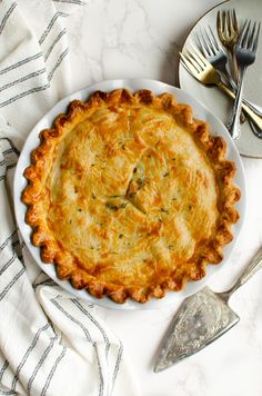 a white plate topped with a pie on top of a table next to silverware