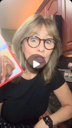 a woman holding up a box with a dog in it's mouth and wearing glasses