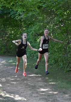 two women running down a dirt road in front of trees